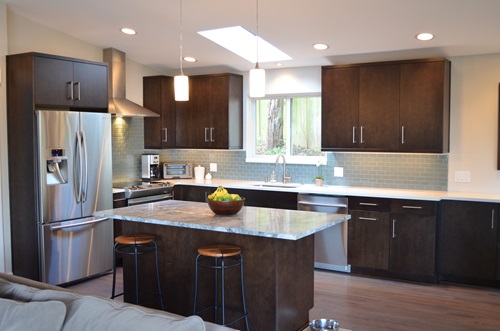 A modern kitchen with dark cabinets, granite countertops, and a stainless steel refrigerator