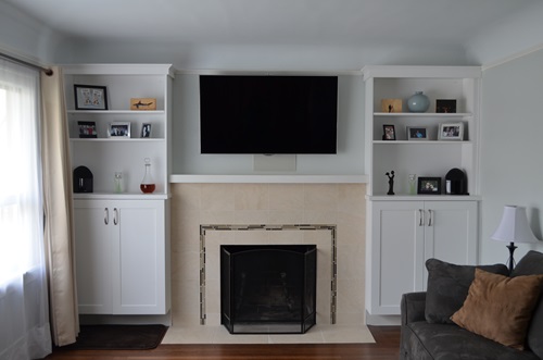 A tiled fireplace with a TV mounted above and bookshelf cabinets on both sides